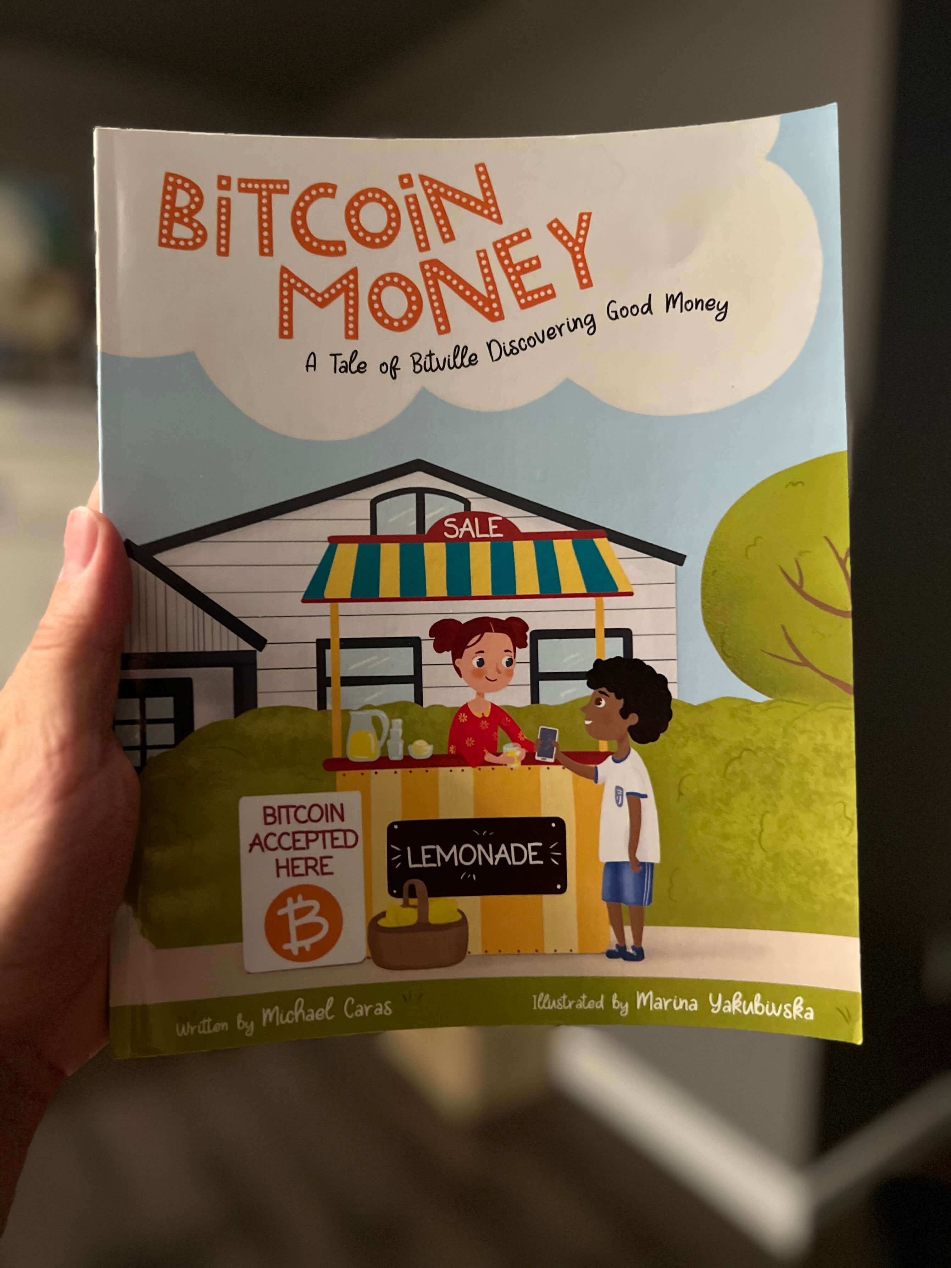 Holding a copy of the children's book Bitcoin Money: A Tale of Bitville Discovering Good Money.