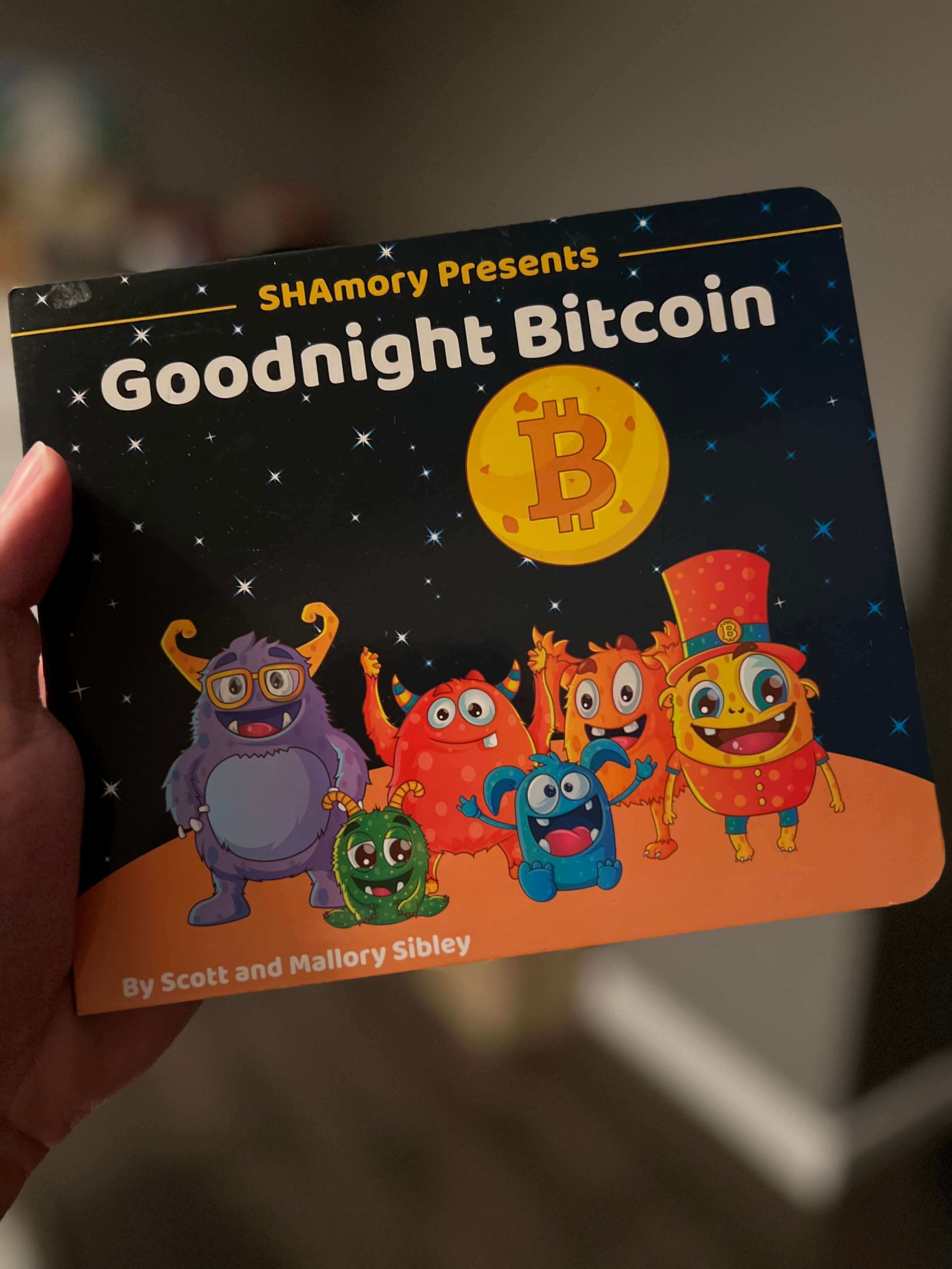 Holding a copy of the children's book Goodnight Bitcoin presented by SHAmory.