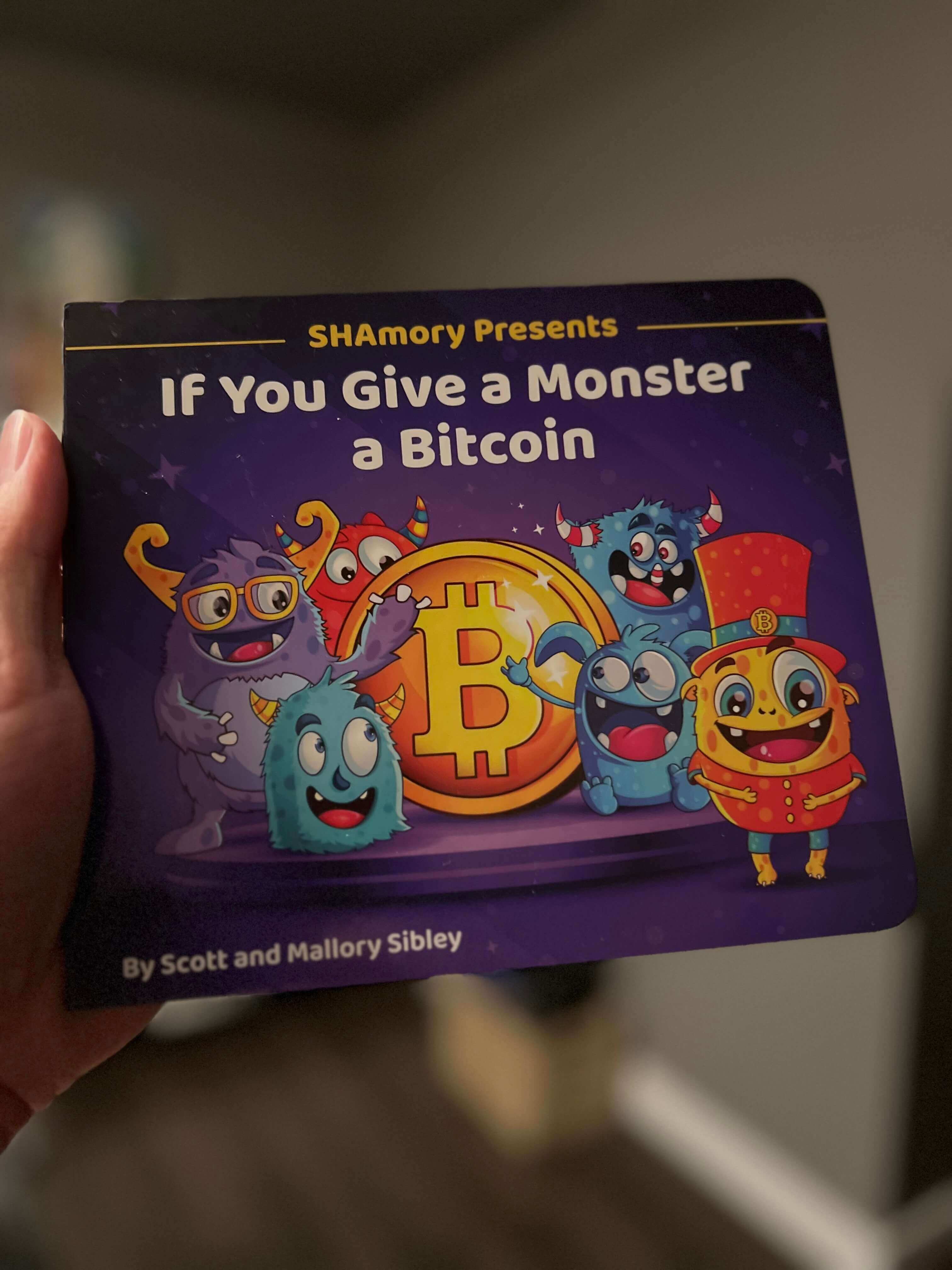 Holding a copy of the children's book If You Give a Monster a Bitcoin presented by SHAmory.